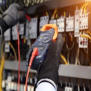Electrical engineer using digital multimeter to check current voltage at circuit breaker in main distribution board.