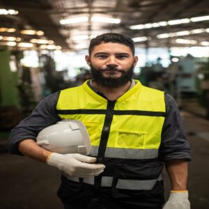 Close-up portrait of Happy latin mix race man worker have unkempt beard in safety uniform holding hard hat wearing vest and glove in industrial manufacturer factory.